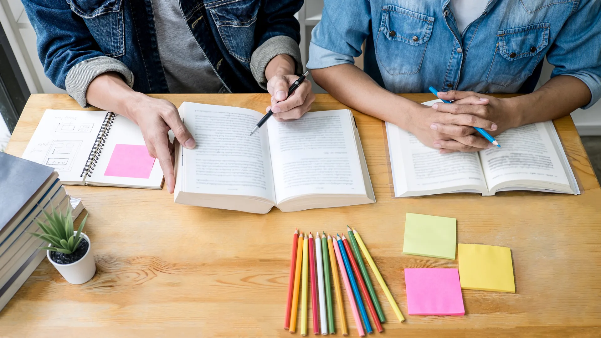 İki lise öğrencisi masada kitap ve renkli kalemlerle birlikte ders çalışıyor